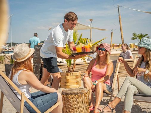 Bedienung serviert Cocktails an eine Gruppe in der Beachlounge